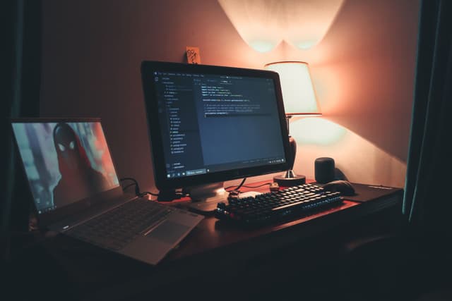 Uma mesa às escuras, só a luz do monitor com código aberto e um post-it escrito "DO IT": o produto continua rodando enquanto ninguém está olhando.