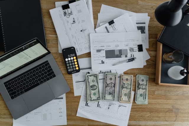Laptop, relatórios financeiros e dinheiro sobre a mesa: os números pelos quais um negócio é pesado.